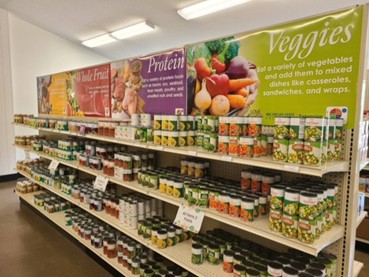 A grocery store aisle with shelves of canned and jarred food and banners reading 